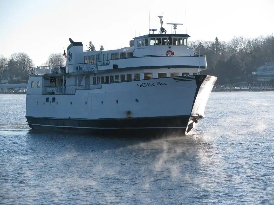 Large white ferry named EMERALD ISLE moving through calm water near a wooded shoreline.