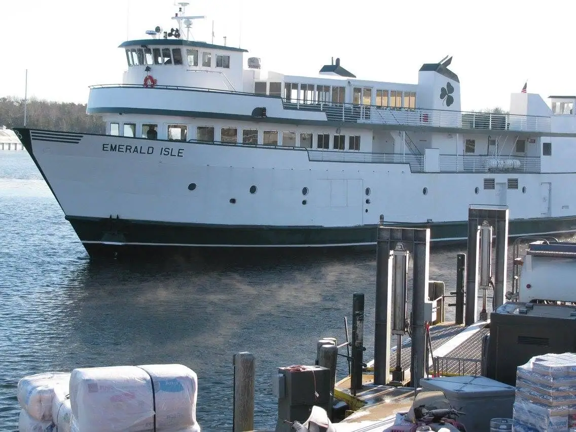 Large white ferry marked “EMERALD ISLE” beside a dock with wrapped cargo and loading equipment.