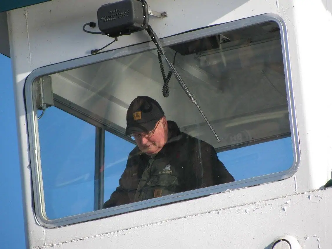 A uniformed man is seen through a ship's window beneath a mounted wiper motor.