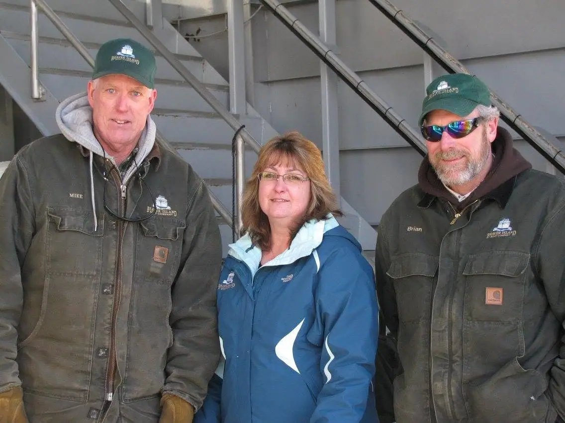 Three adults pose in work clothing before a gray metal staircase and railings.