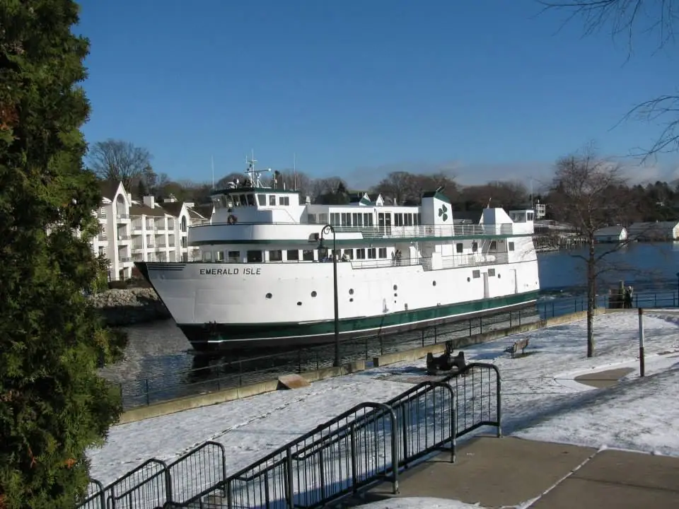 A white ferry beside a snow-covered waterfront with black railings and buildings behind it.