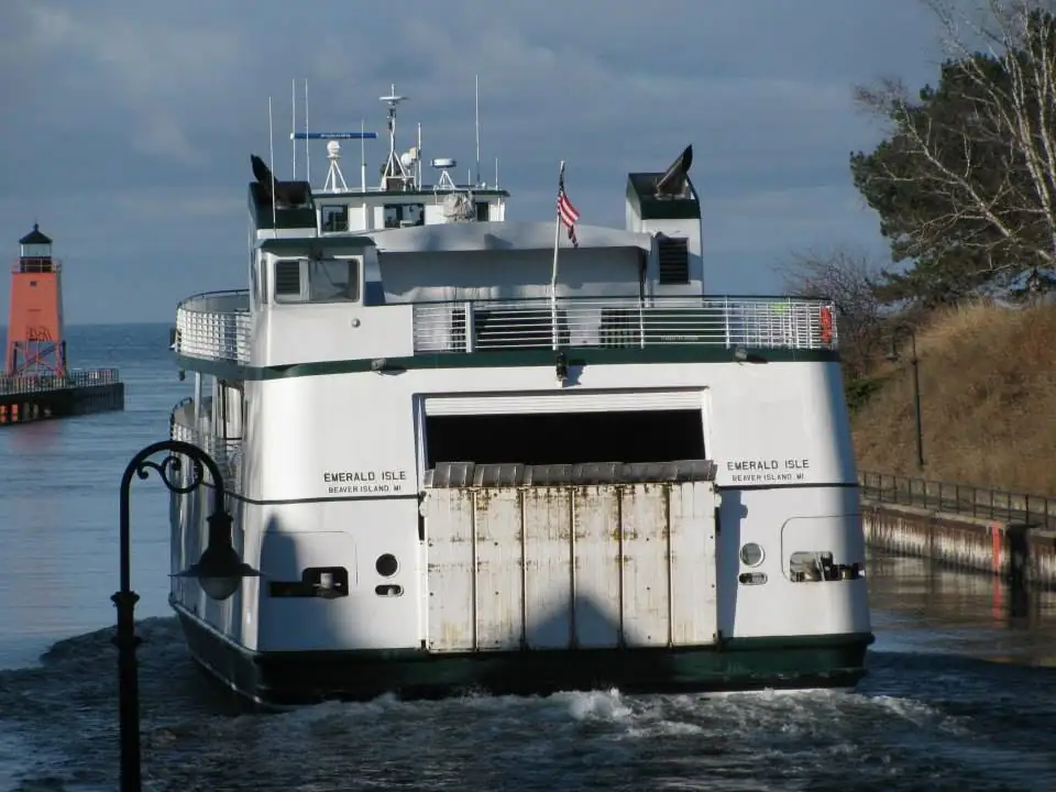A white ferry approaches a dock beside a red lighthouse, viewed from directly behind.