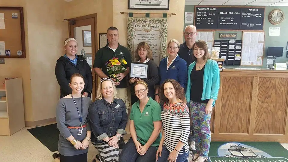 Ten people pose inside a ticket office, with a bouquet, framed certificate, fare boards, and an Irish blessing banner.