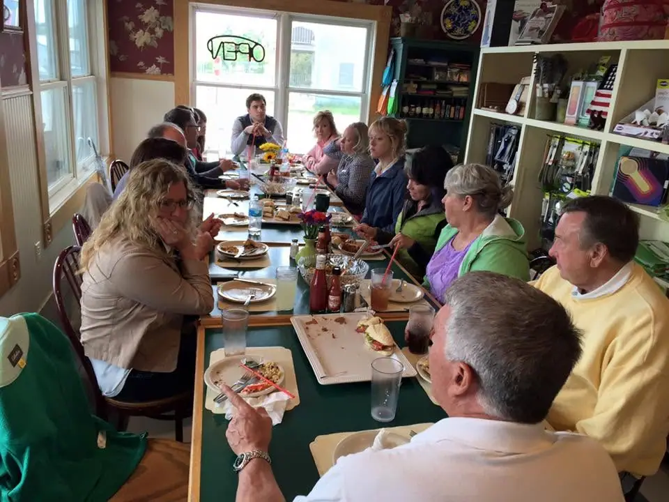 Adults sit around a long table during a shared meal in a brightly lit dining room.