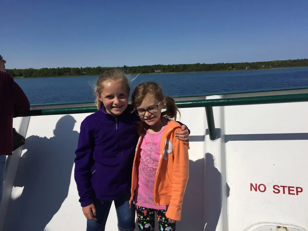 Two girls pose together on a passenger vessel deck beside a railing and a visible “NO STEP” warning.