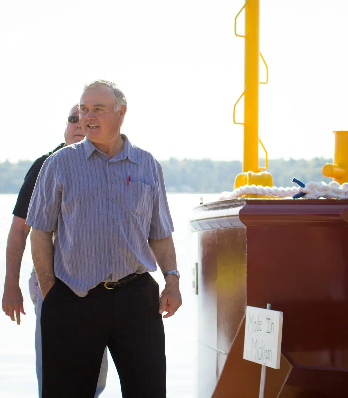 Two men stand on a boat deck beside a yellow mast and a sign reading “Made In Michigan.”