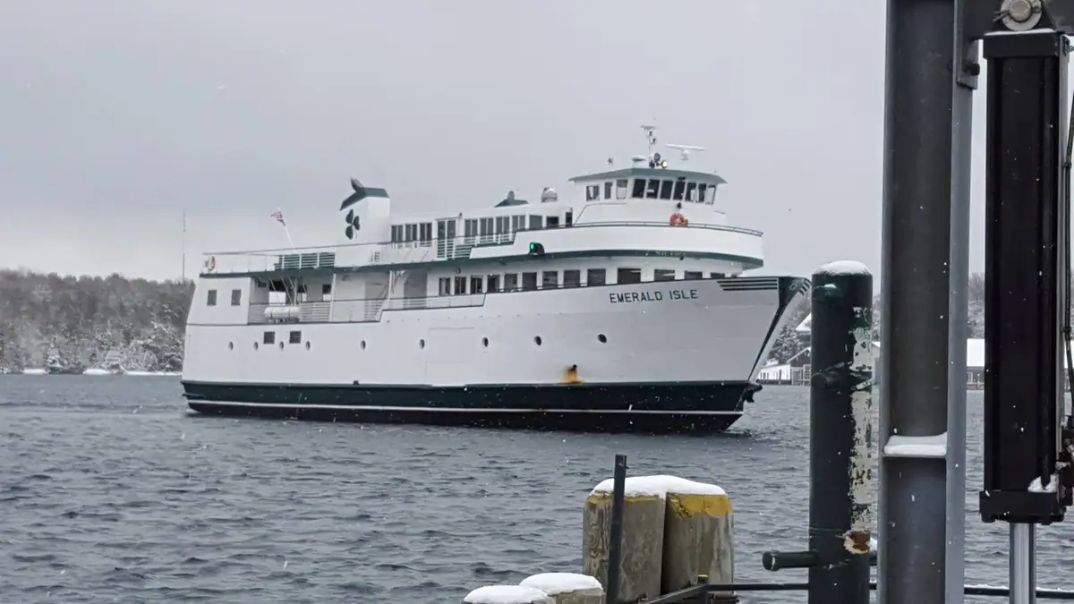A white passenger ferry passes snow-covered wooden pilings beneath an overcast sky.