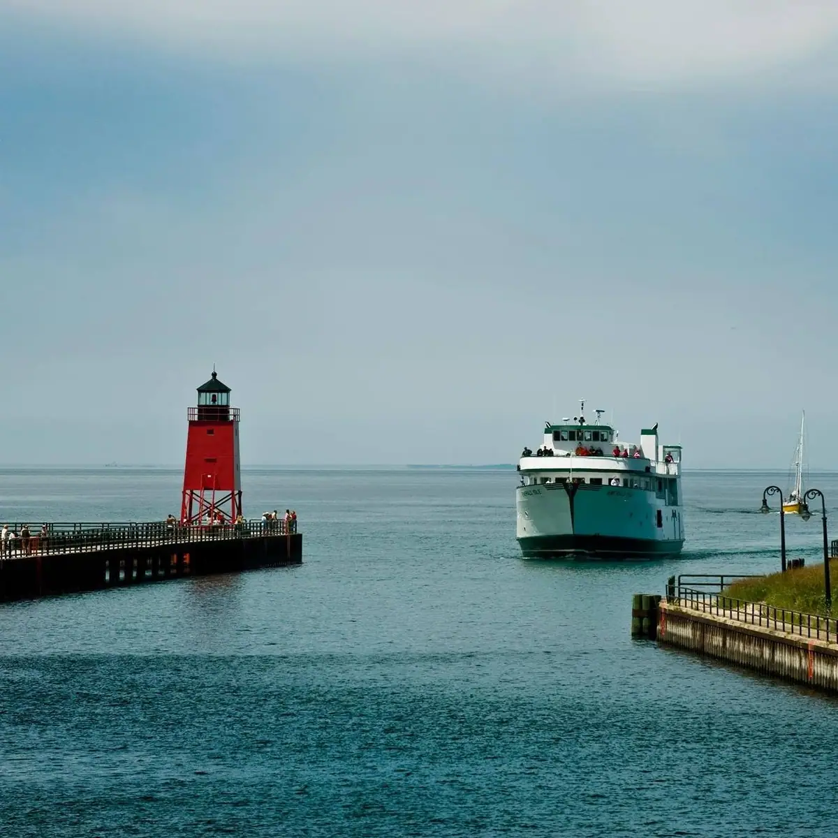 A passenger ferry approaches between a red lighthouse pier and a concrete waterfront pier.