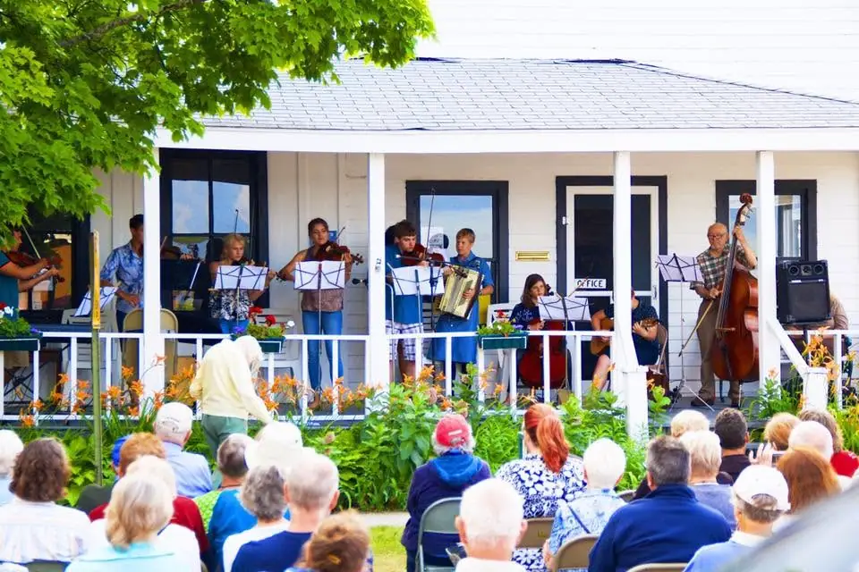 Musicians perform on a porch before a seated audience.