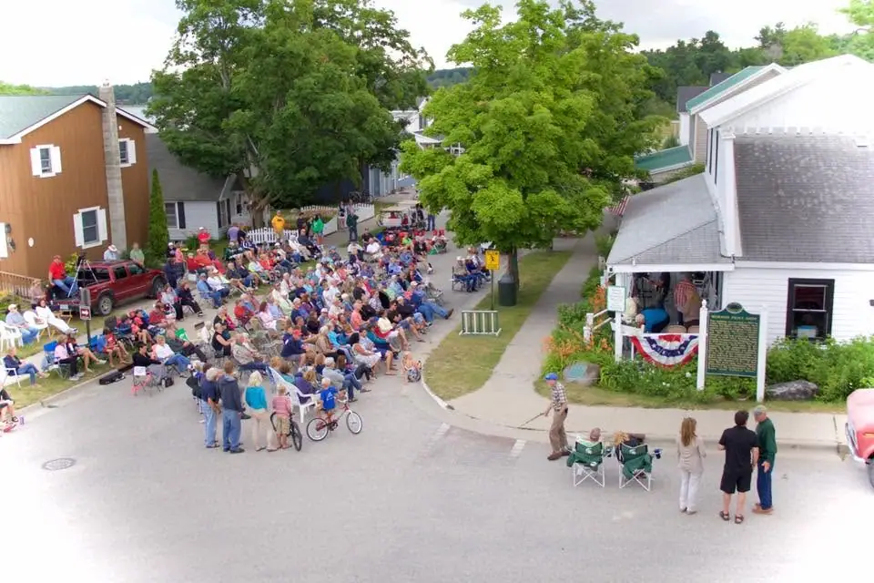 Elevated view of a large crowd seated in lawn chairs along a street beside historic-looking buildings.
