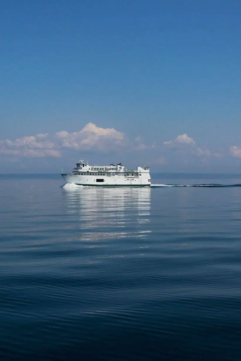 White passenger ferry crossing calm water beneath a blue sky with scattered clouds.