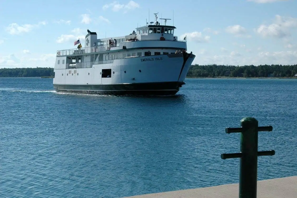 A white passenger ferry named EMERALD ISLE travels past a waterfront bollard.
