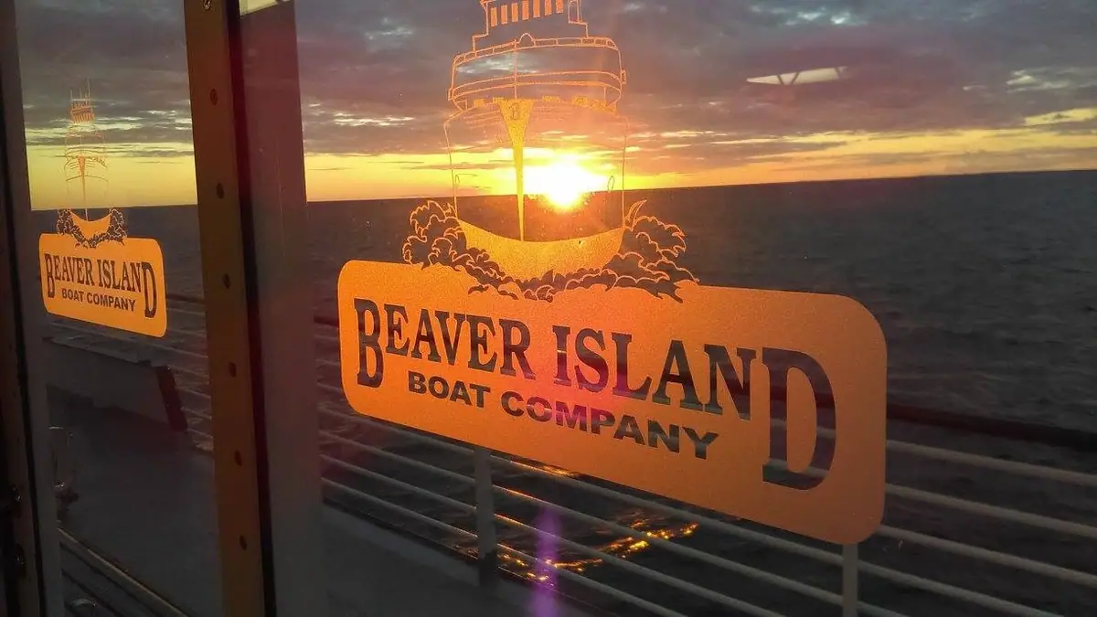 A boat-company logo decal glows on a window against a sunset over open water.