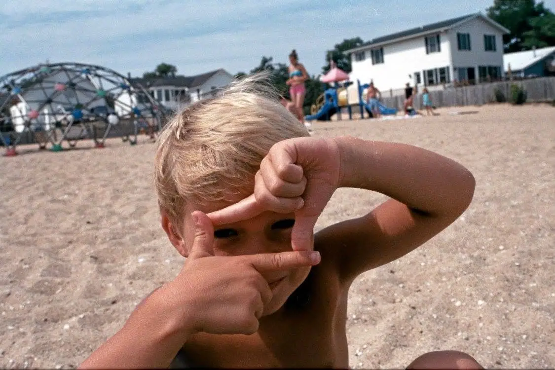 A child makes a frame with their fingers in front of a sandy playground.
