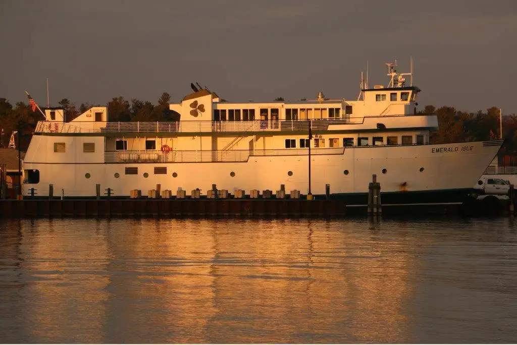 A white passenger ferry named EMERALD ISLE is moored at a pier in warm evening light.