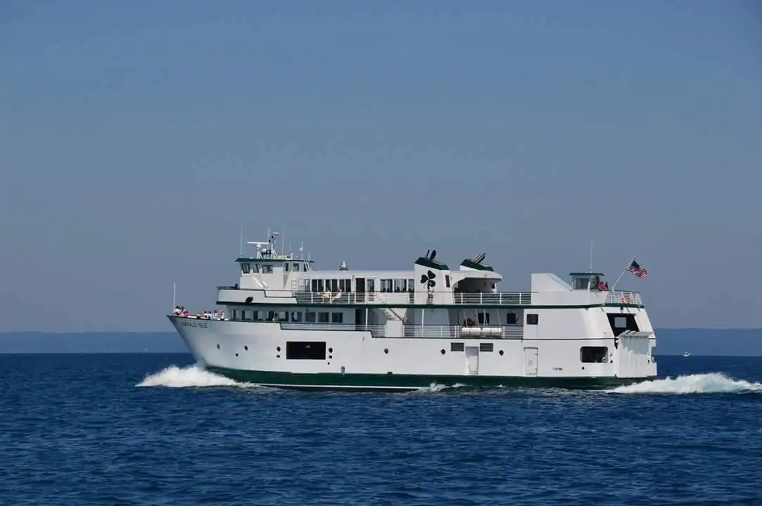 White passenger ferry with green trim travels across open water, leaving a foamy wake.