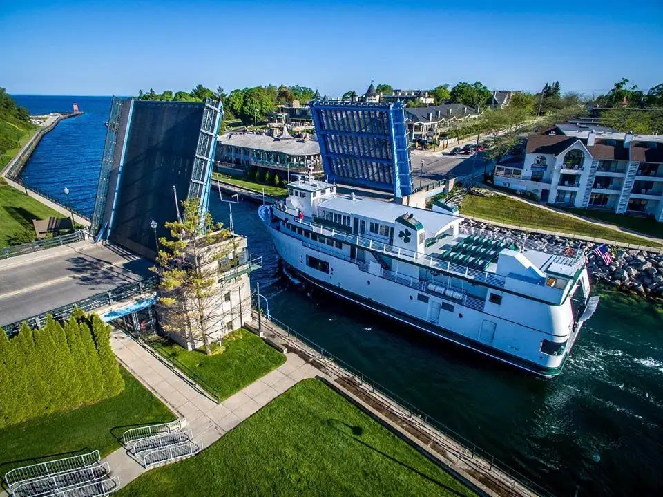 Aerial view of a white ferry passing between the raised leaves of a drawbridge.