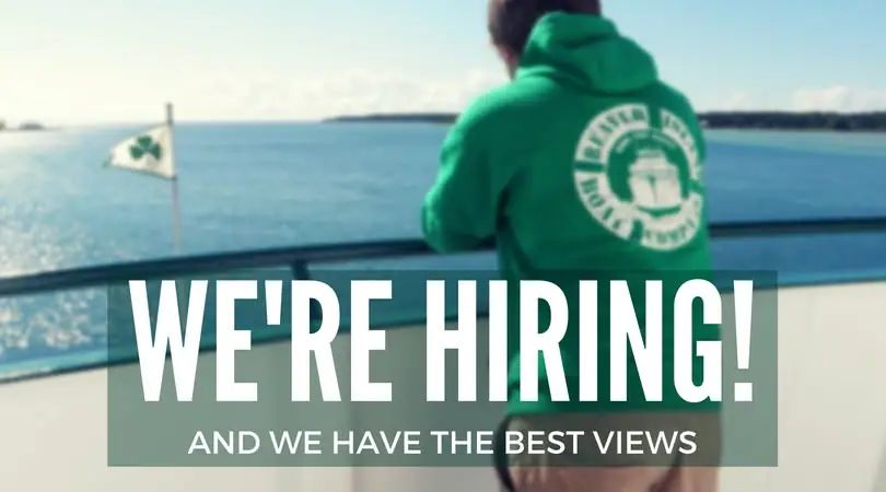 A person in a green hoodie overlooks the water from a vessel deck beneath a hiring message.