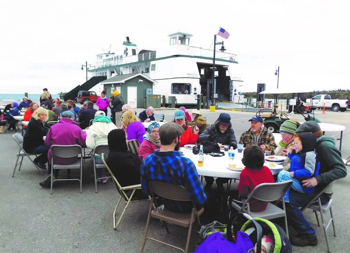A group eats at outdoor tables beside a ferry docked behind them.
