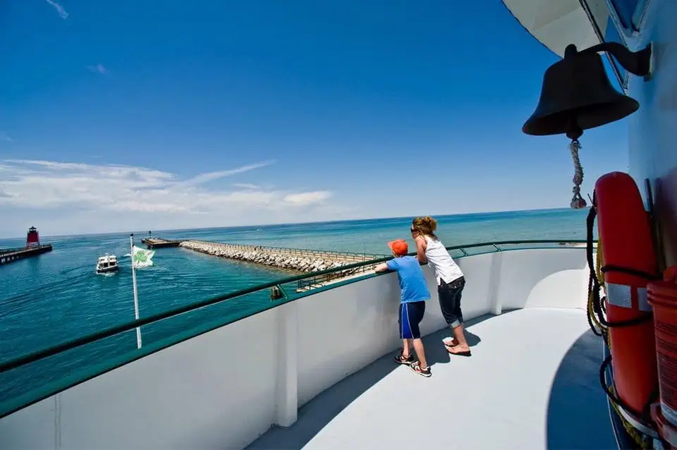 Two children watch a small boat near a breakwater from the deck of a vessel.