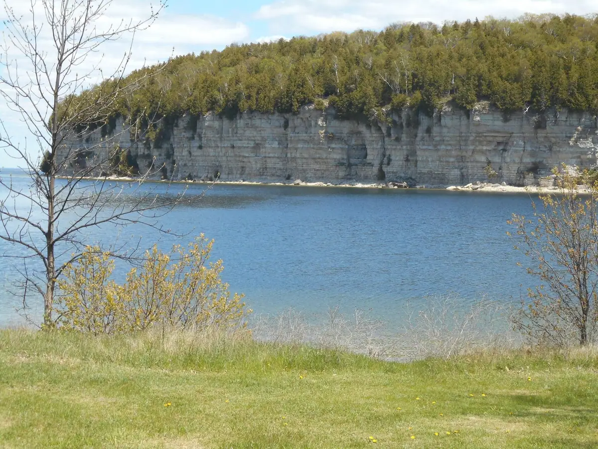 Layered rock cliff and wooded shoreline across calm blue water.