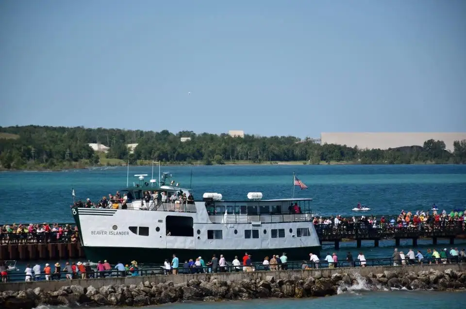 A white passenger ferry crowded with people lies alongside a pier as onlookers gather along the waterfront.