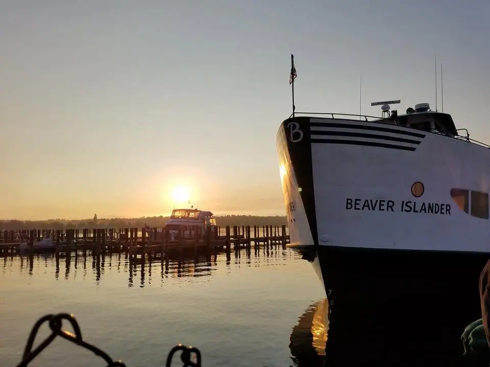 White ferry beside a pier at sunset, with a smaller boat and reflections on the water.