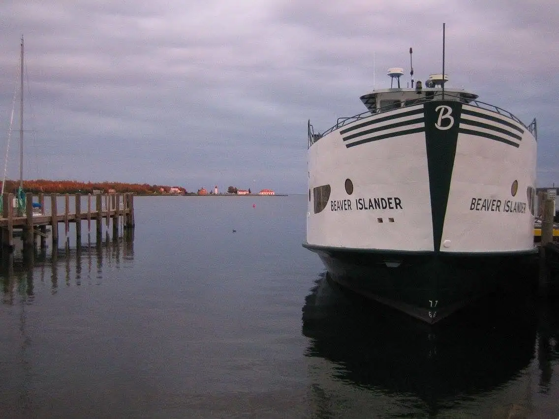 A white ferry with black trim is moored beside a wooden pier under a cloudy sky.