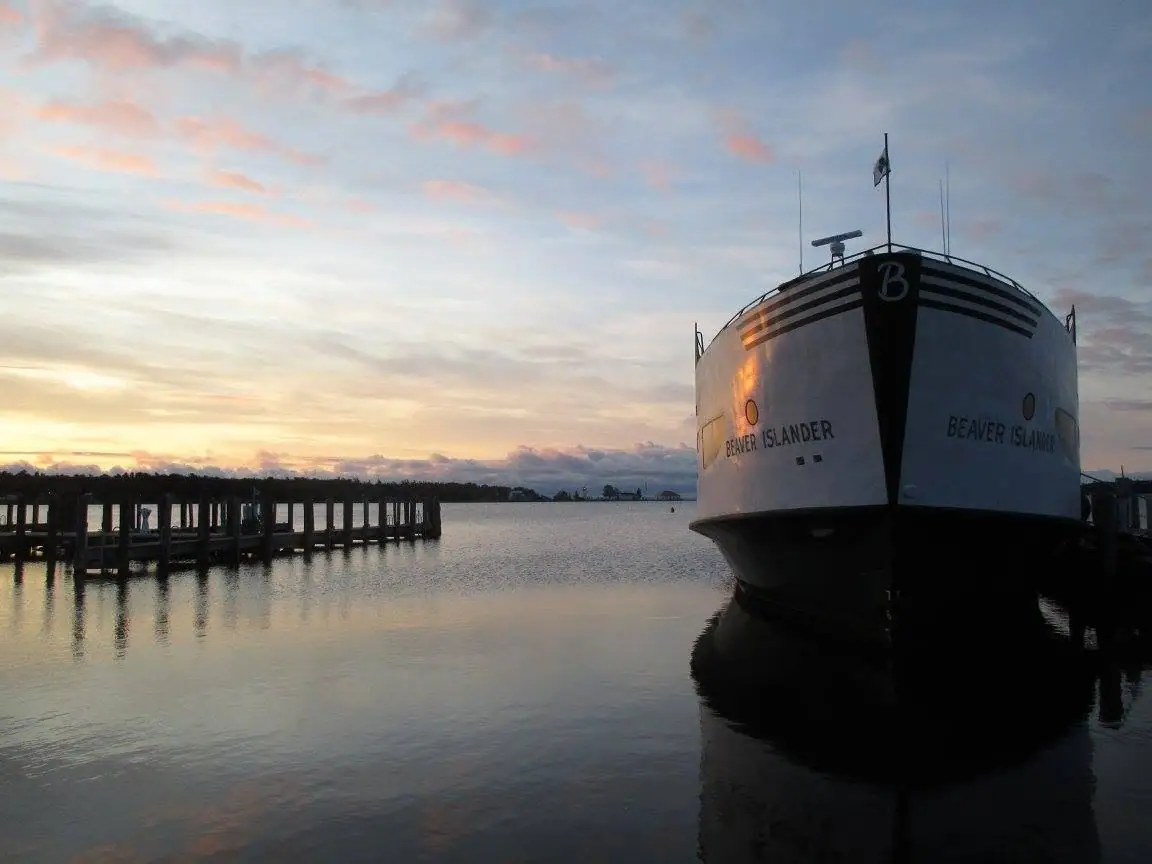 A white ferry with a black bow is moored beside a pier at sunset.
