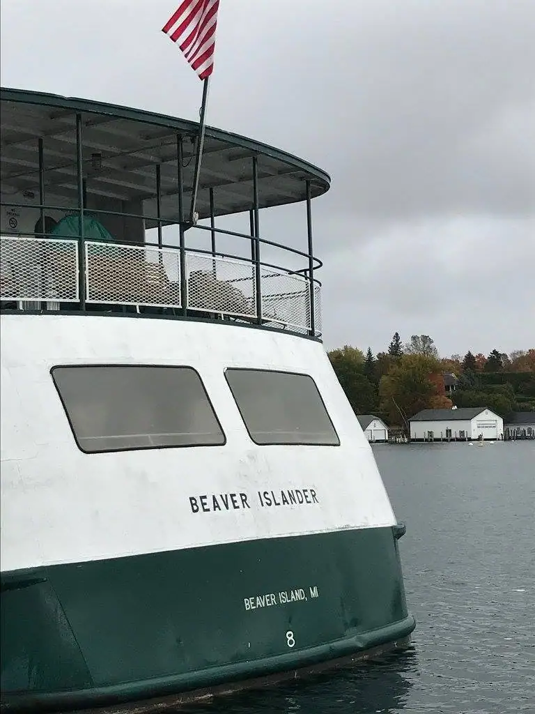 Close view of a green-and-white ferry stern with an American flag, moored beside waterfront buildings.
