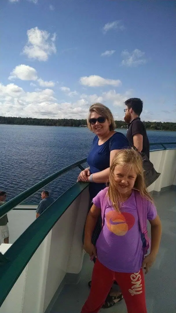 A woman, a girl, and a man stand on a passenger-vessel deck above open water.