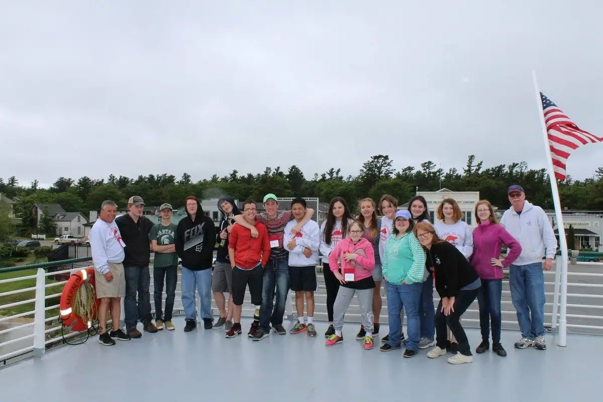 A group of people poses on a vessel deck beside a life preserver and an American flag.