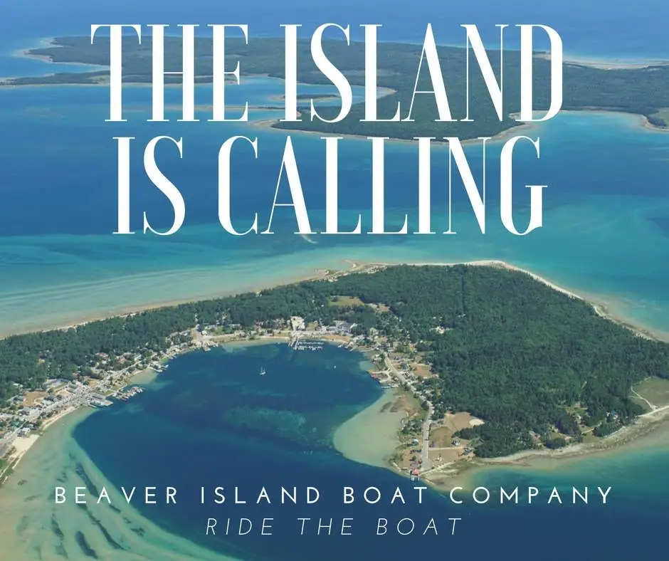 Aerial promotional photograph of a wooded shoreline, settlement, harbor, and surrounding blue water.