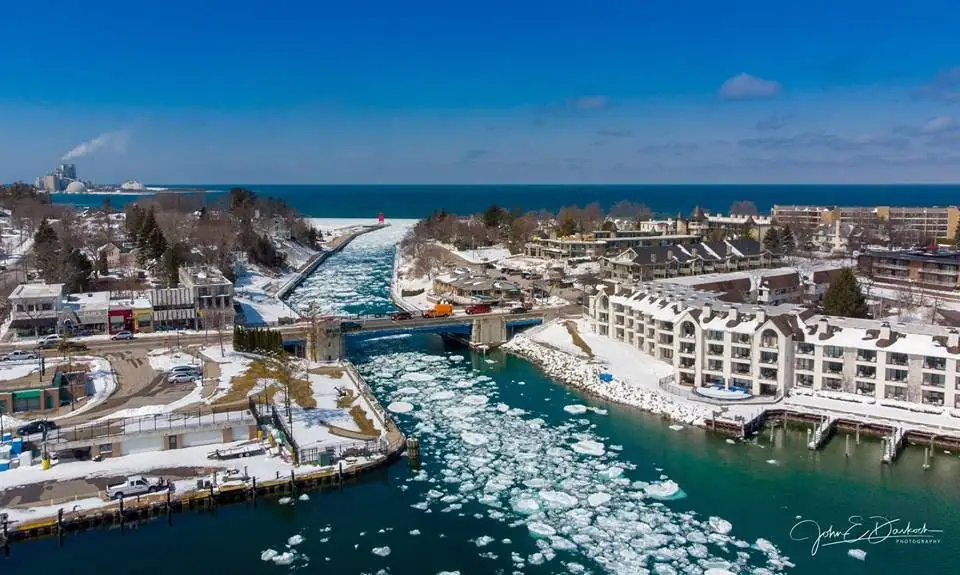 Aerial winter view of an ice-filled harbor channel, bridge, waterfront buildings, roads, and docks.