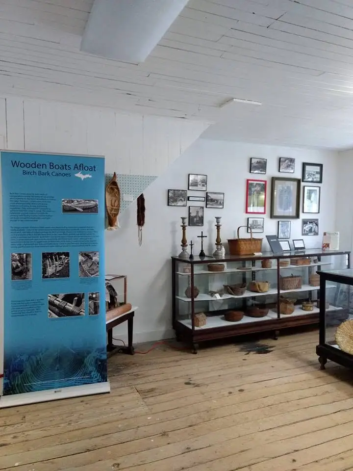 Museum interior with a birch-bark canoe exhibit, display cases, framed photographs, and baskets.