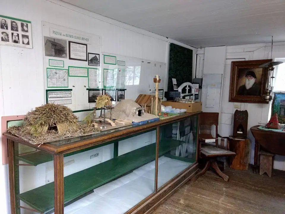 Photograph of a small historical exhibit room with display cases, wall panels, portraits, and artifacts.