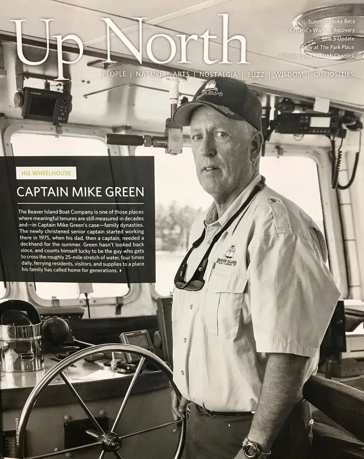 A black-and-white magazine page shows a uniformed man standing beside a ship's wheel in a wheelhouse.