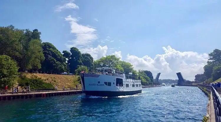 A passenger ferry passes beneath a raised drawbridge on a sunny waterway.