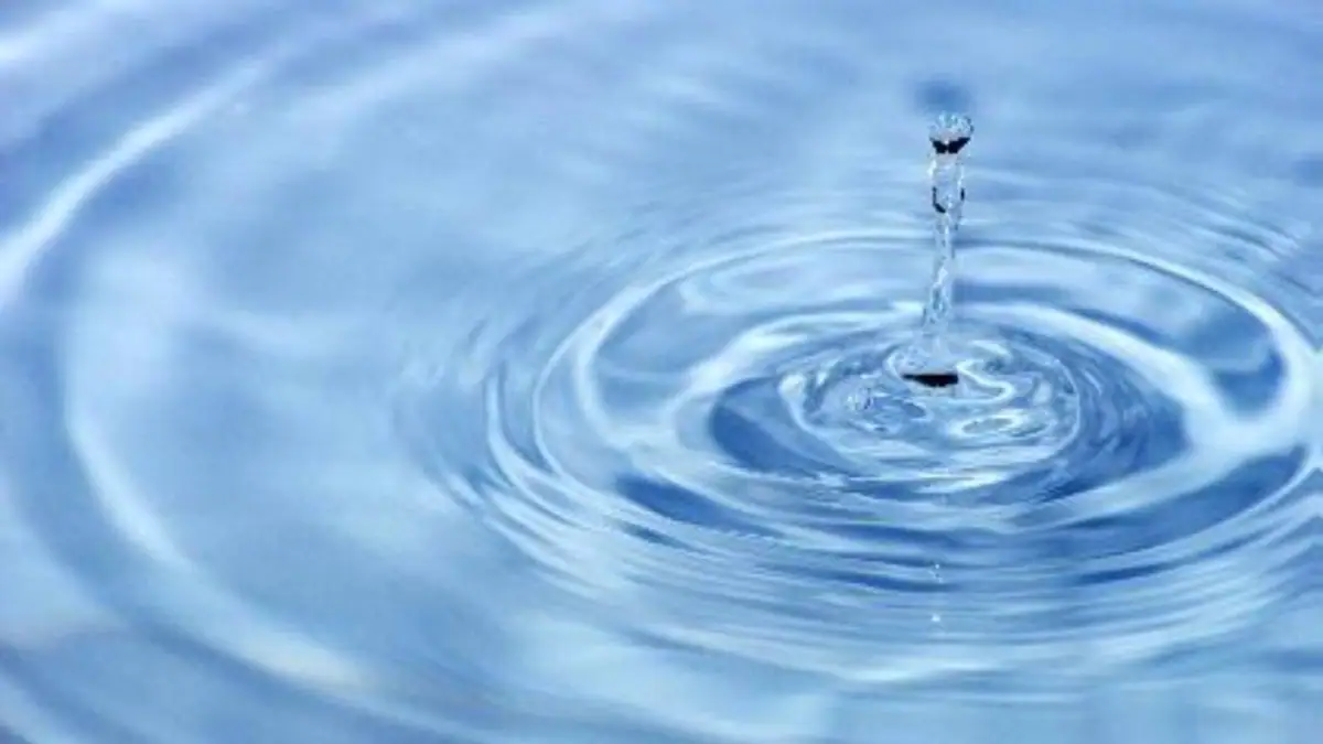 A water droplet strikes a blue surface, creating overlapping circular ripples.