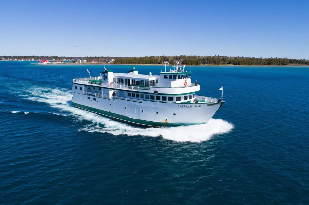 A white-and-green passenger ferry cuts through blue water, leaving a broad white wake.