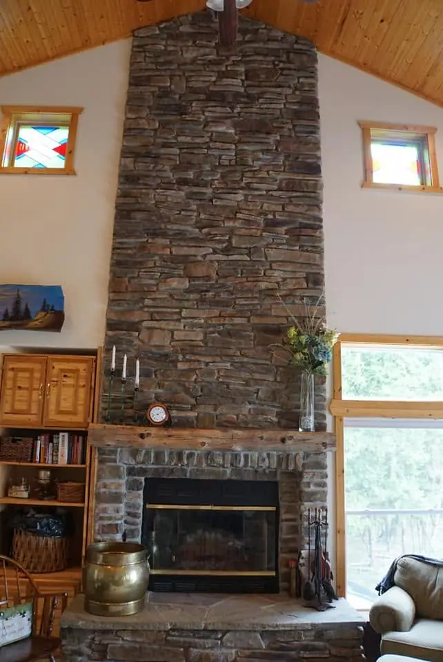 A tall stone fireplace with a wooden mantel stands beneath a vaulted wood-paneled ceiling.
