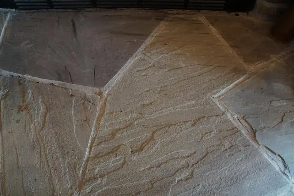 Close-up photograph of a rough, tan-colored surface divided by pale seams and branching cracks.