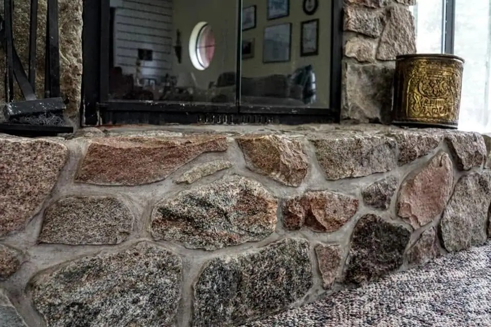 Close view of a split-stone fireplace with black glass doors, tools, and a decorative metal container.