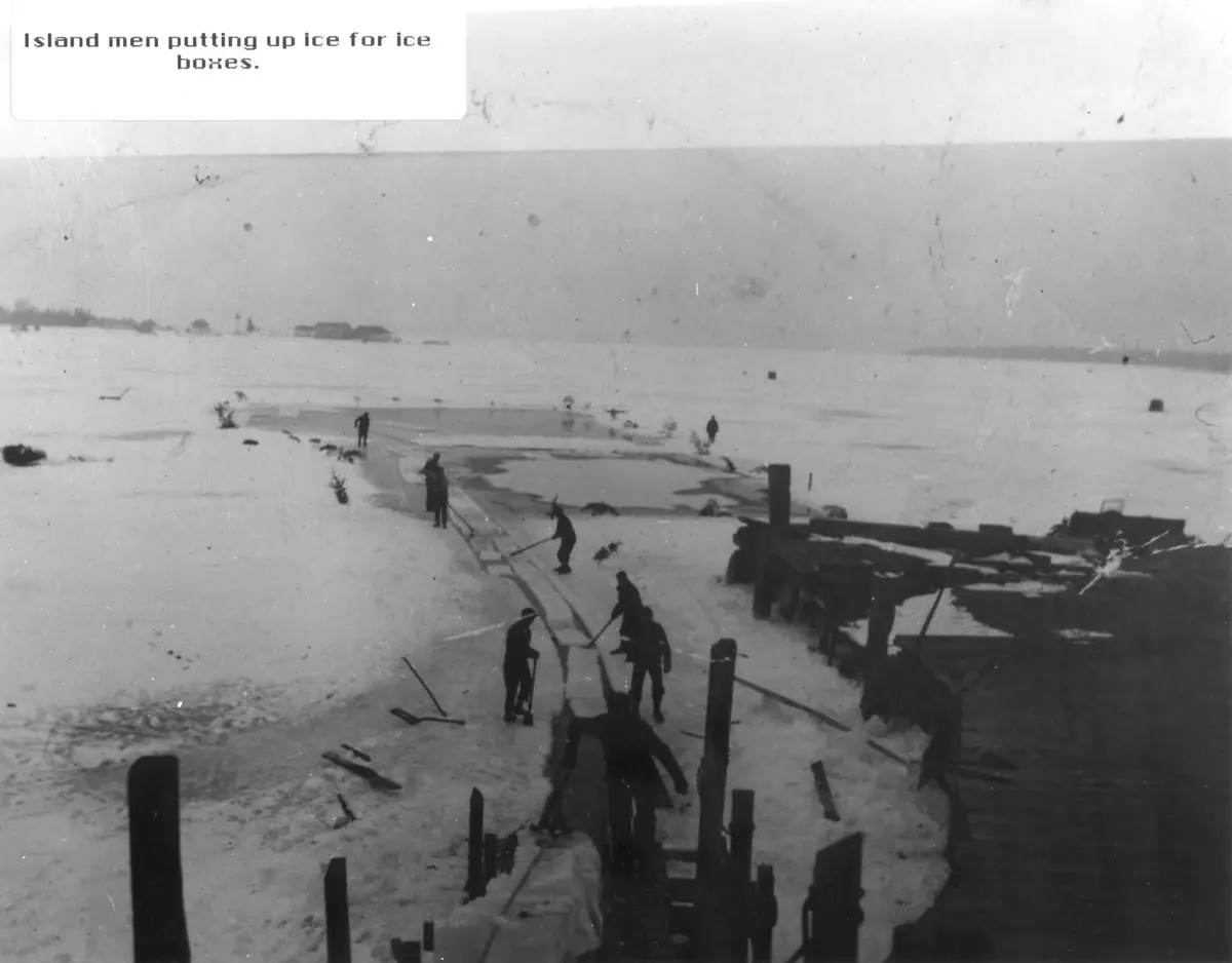 Men work across a frozen, snow-covered expanse beside wooden structures and cut sections of ice.