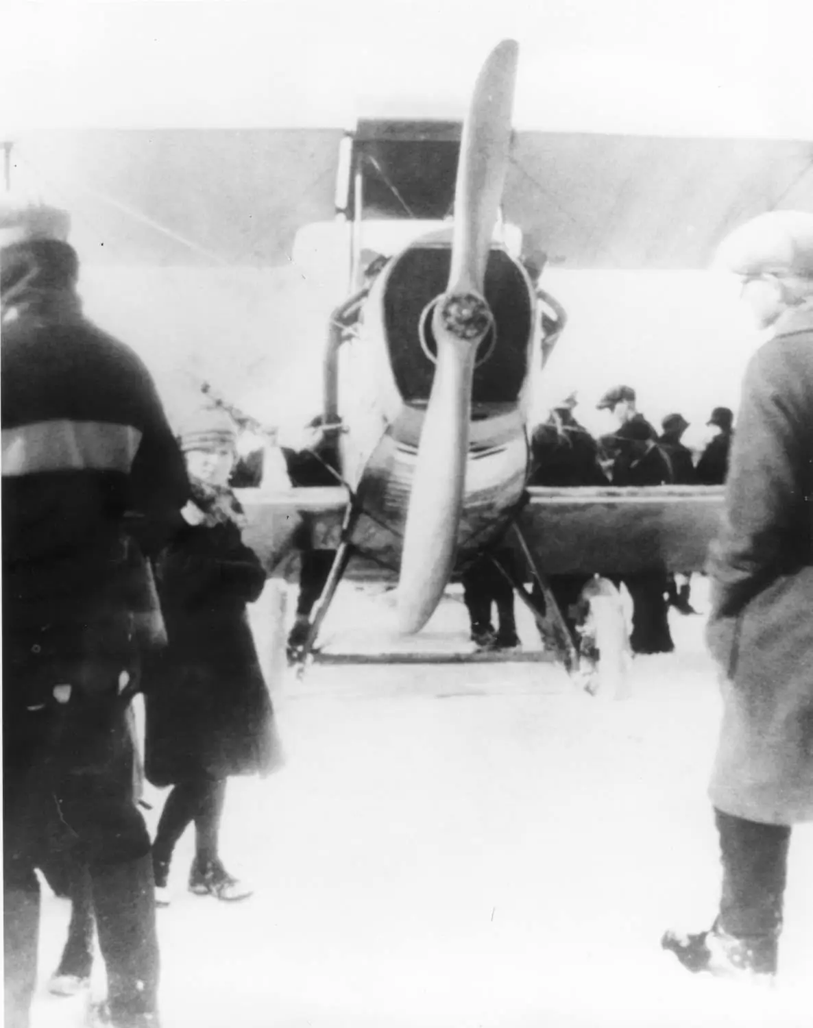 A biplane stands on snow while bundled-up people gather around it.