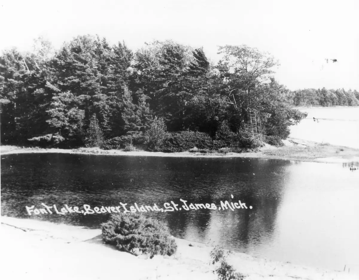 Black-and-white photograph of a wooded shoreline and dark water, with a hand-lettered caption across the foreground.