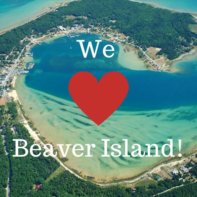 Aerial photograph of a wooded shoreline settlement and blue-green water, overlaid with white lettering and a red heart.