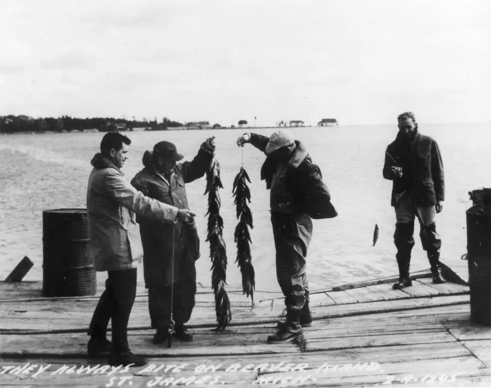Four men display strings of fish on a wooden dock beside the water.
