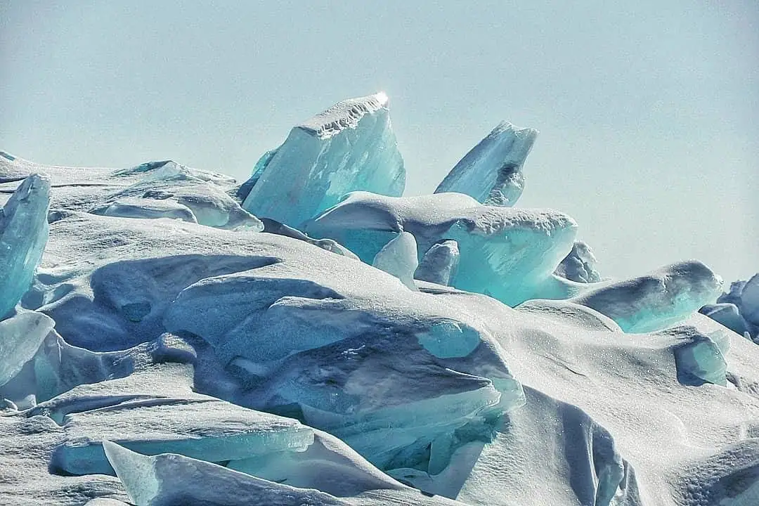 Jagged blue ice slabs rise in overlapping ridges beneath a pale blue sky.