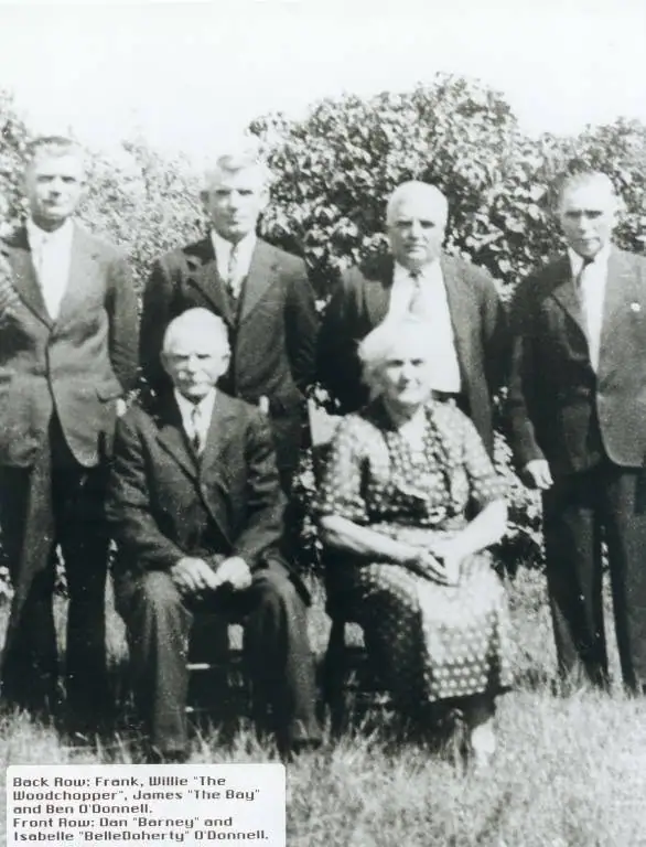 Six people pose outdoors, with four men standing behind a seated man and woman.